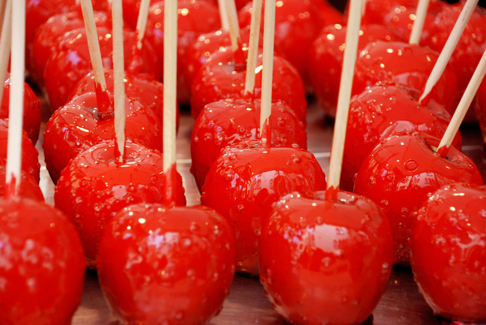 Six glossy red candy apples with wooden sticks on a parchment-lined baking sheet, warm kitchen lighting