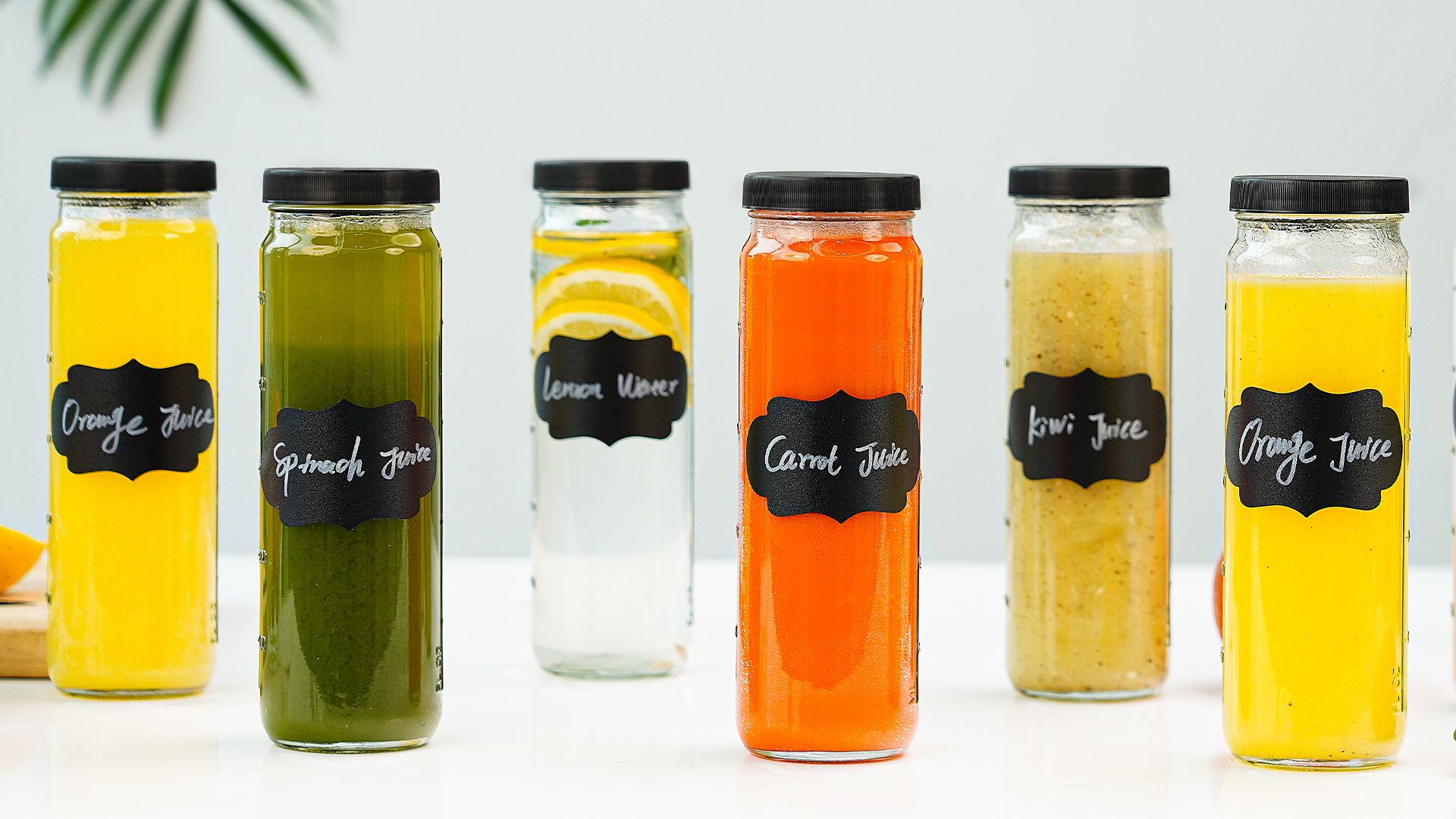 Six mason jars filled with different colorful fresh juices lined up on a bright kitchen counter, each with a simple lid, natural window light
