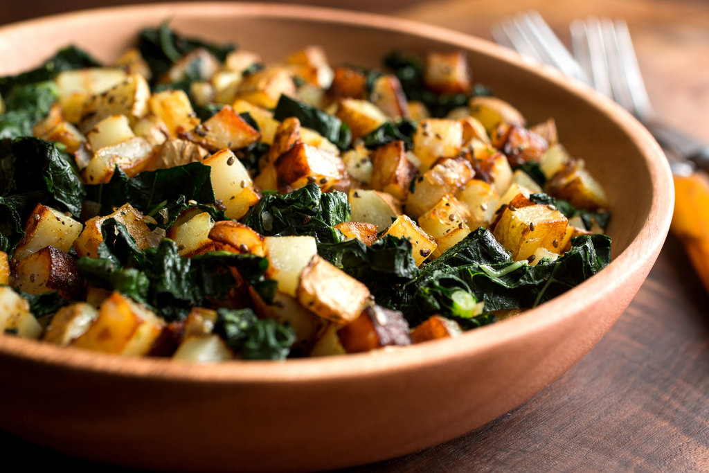 Sliced Yukon Gold potatoes and chopped kale prepped on a cutting board beside a chef’s knife