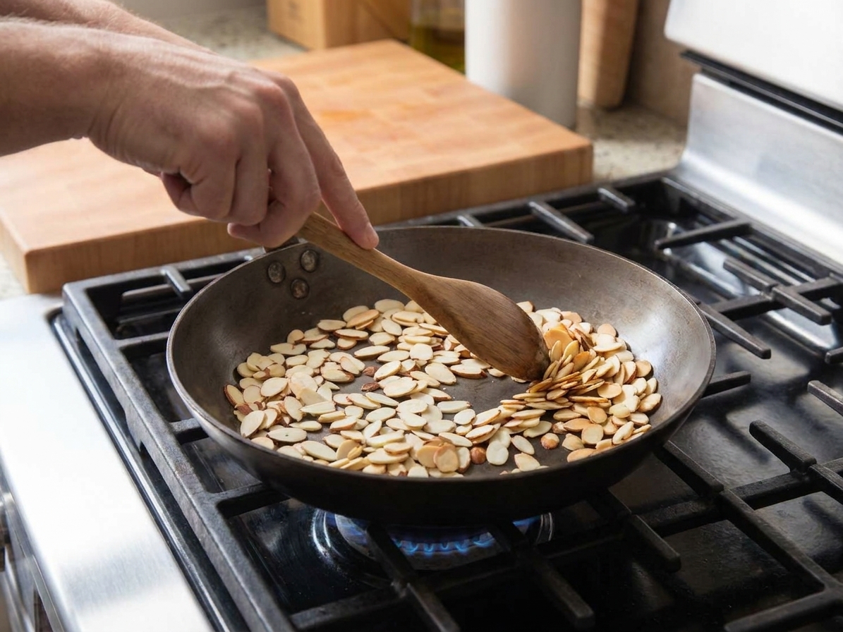 Sliced almonds toasting in a dry skillet on a stovetop, turning lightly golden