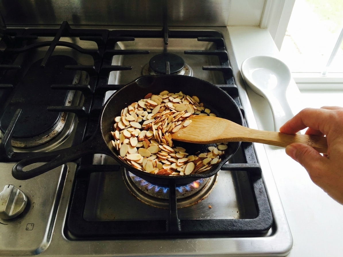 Sliced almonds toasting in a small skillet over medium heat on a home stove