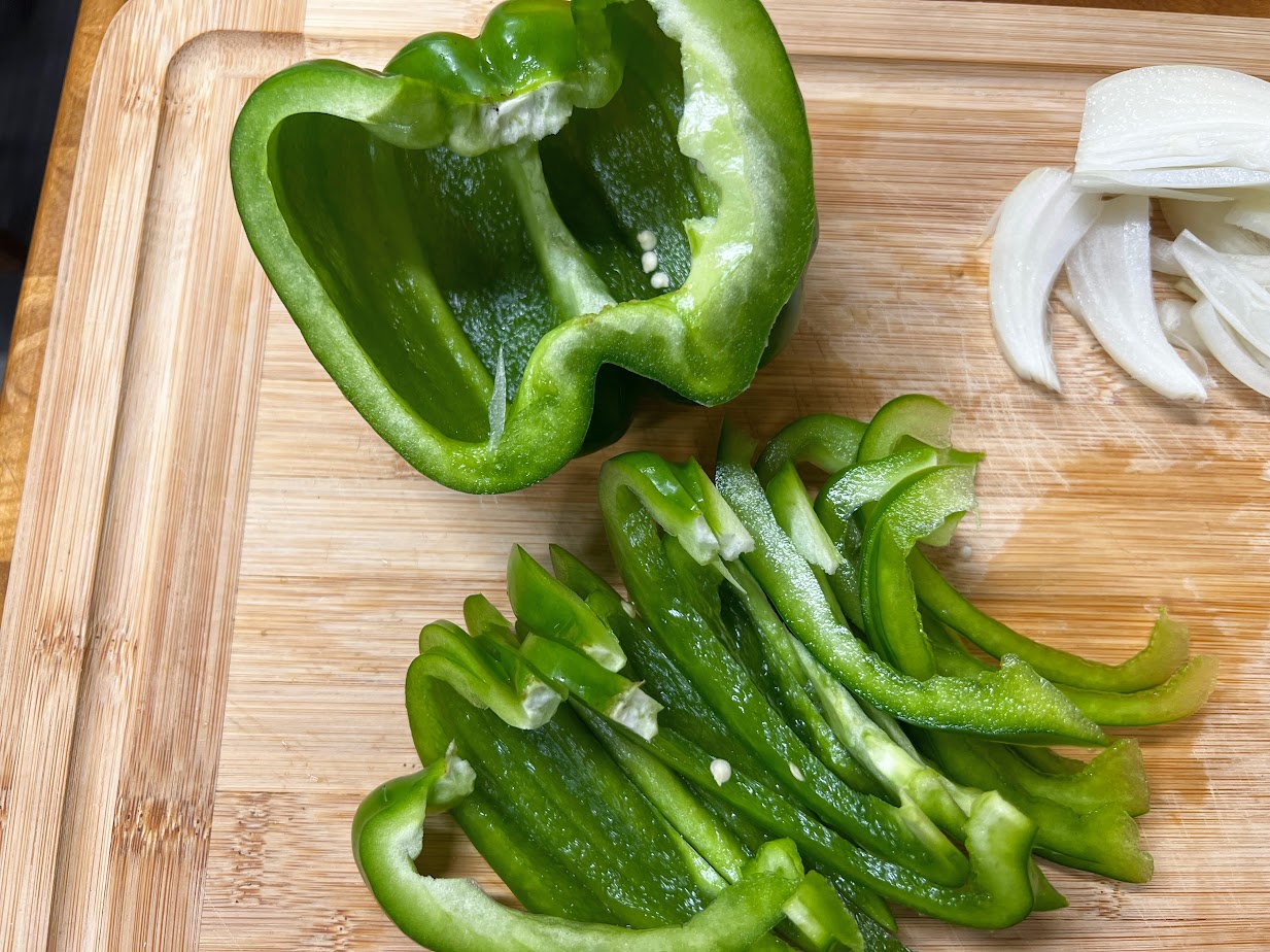 Sliced bell peppers and onions with minced garlic on a cutting board on a home kitchen counter