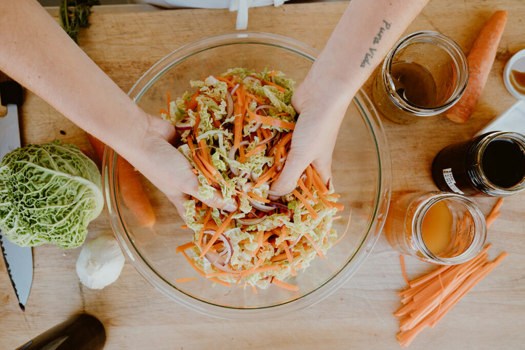 Sliced cabbage, onions, and carrots prepped in separate piles on a cutting board on a bright kitchen counter