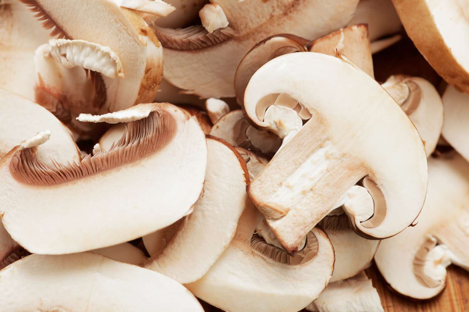 Sliced champignon mushrooms piled on a wooden cutting board with a chef's knife beside them on a home kitchen counter