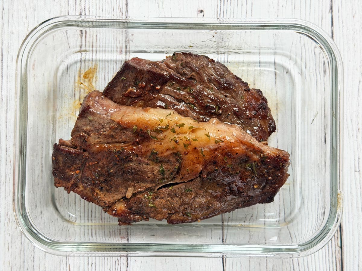 Sliced cooked NY strip steak stored in a glass meal prep container with a tight lid on a kitchen counter