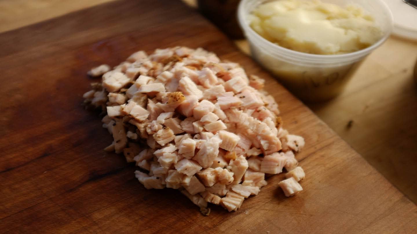 Sliced cooked turkey arranged in a glass storage container with a small amount of broth on the bottom on a kitchen counter
