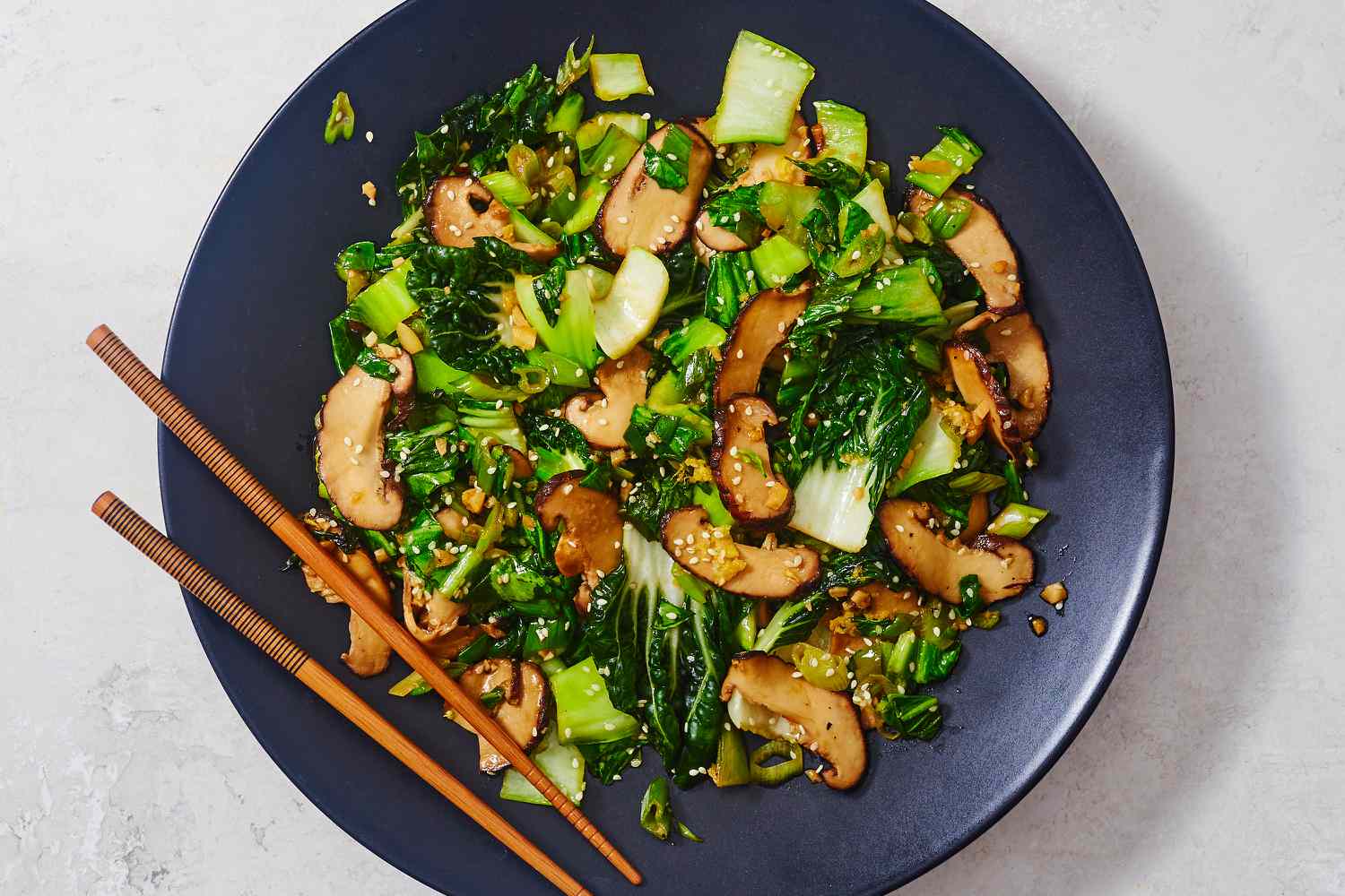 Sliced cremini mushrooms and chopped baby bok choy on a cutting board with a knife in a home kitchen