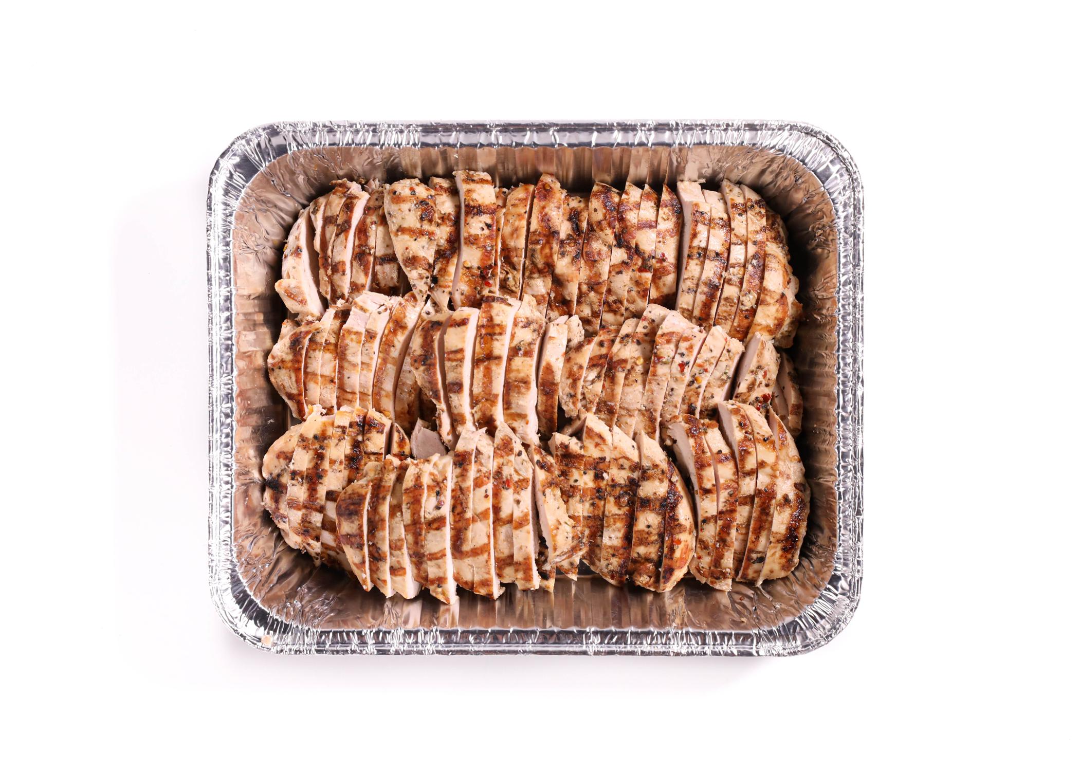 Sliced grilled chicken arranged in a meal prep container with herbs on top on a clean kitchen counter