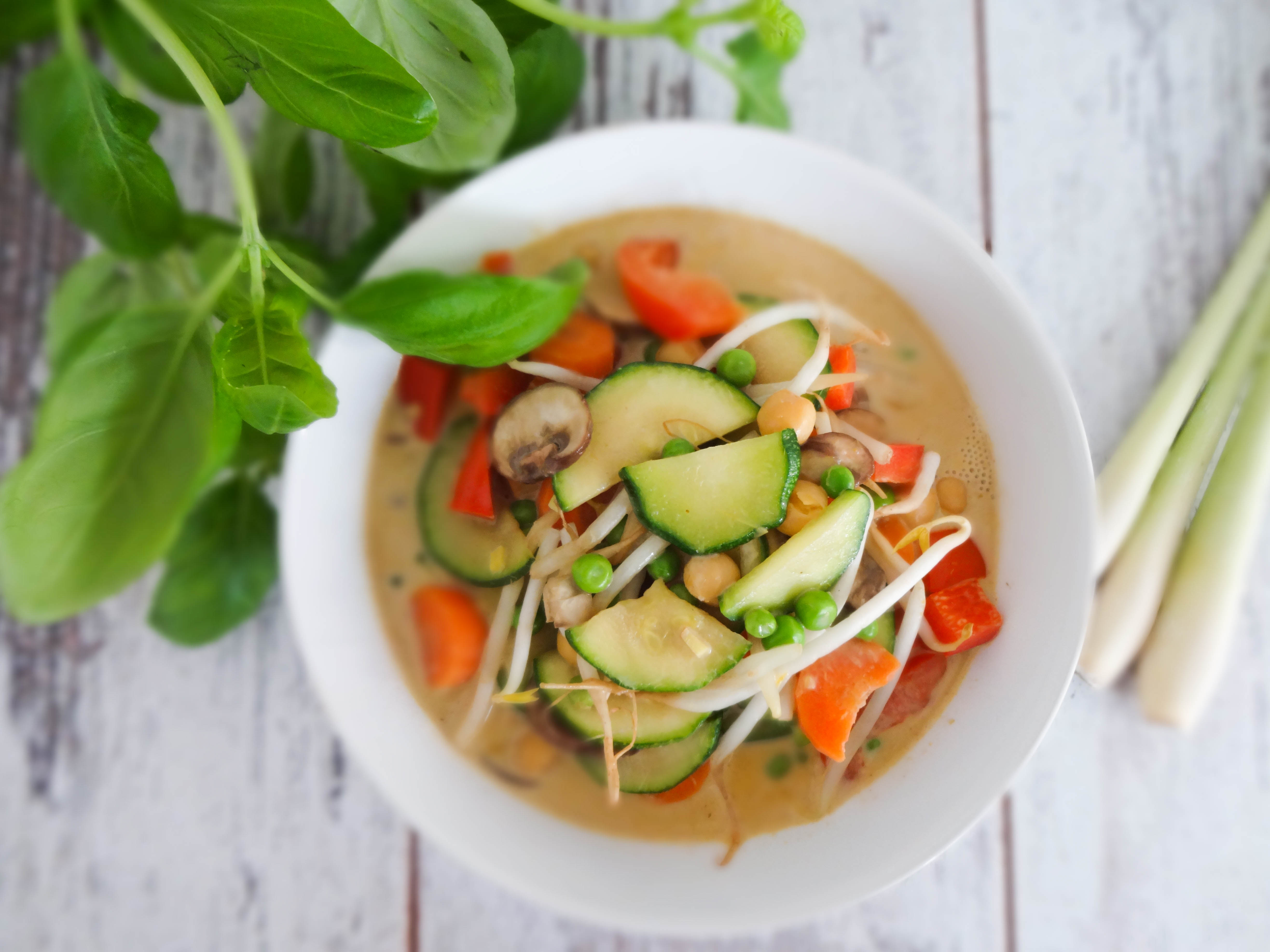 Sliced lemongrass, chopped shallots, garlic cloves, and red curry paste portioned in small bowls on a warm-toned kitchen counter