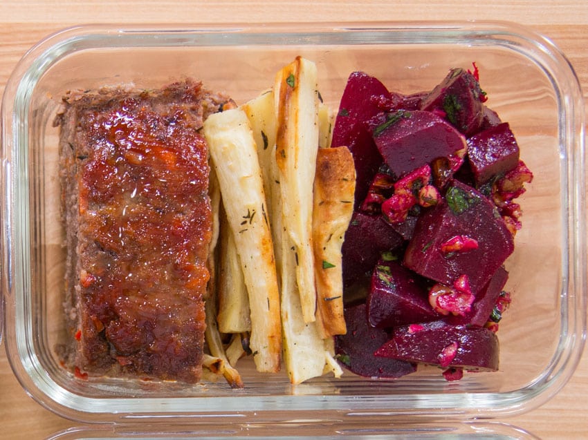 Sliced meatloaf arranged in a glass meal prep container with a little sauce pooled at the bottom on a kitchen counter