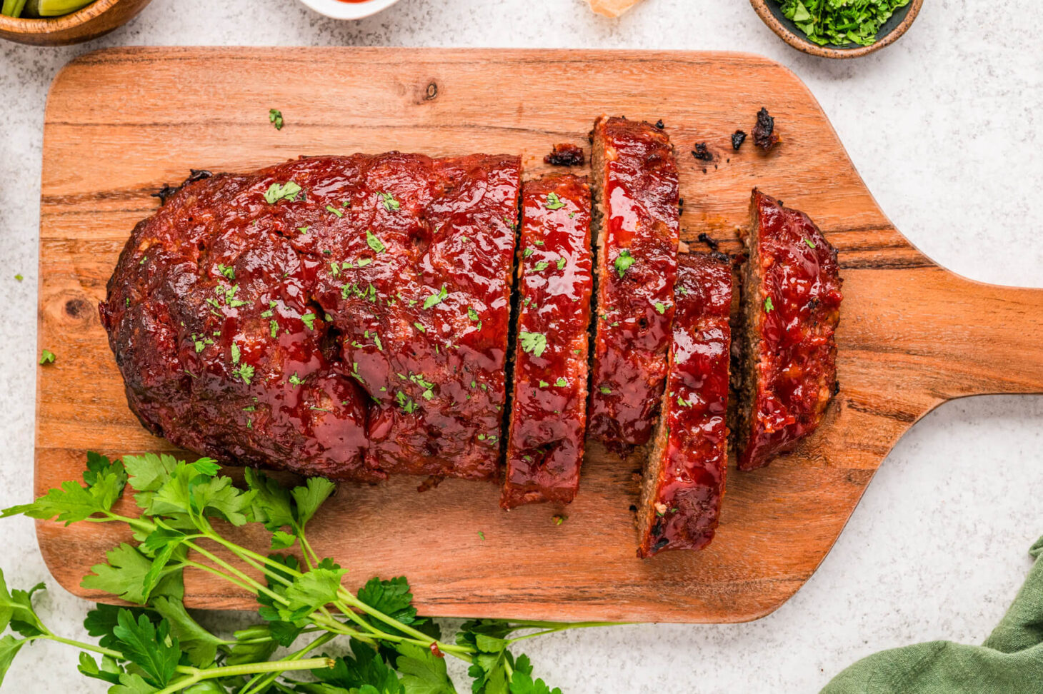 Sliced meatloaf on a wooden cutting board with a moist crumb and shiny glaze on a kitchen counter