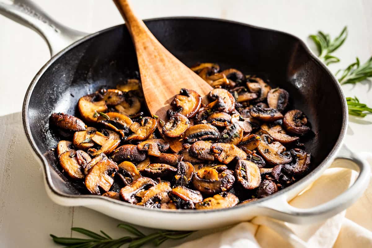 Sliced mushrooms browning in a skillet with butter, showing golden edges and a few darker caramelized spots