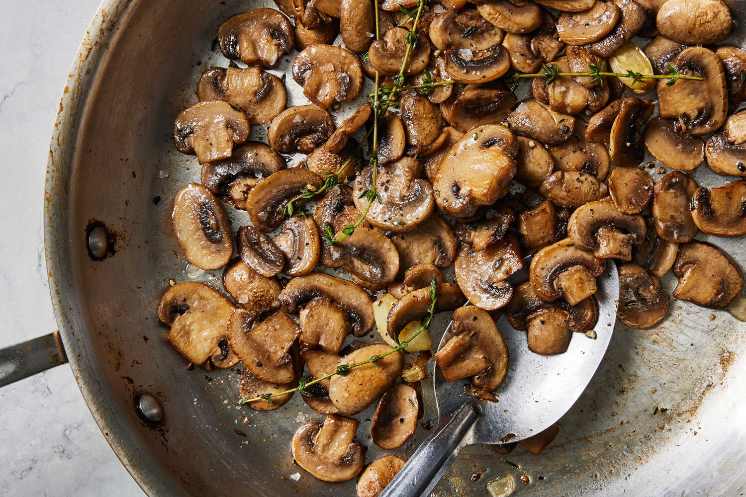 Sliced mushrooms browning in butter in a stainless steel skillet on a home stove, steam rising in warm kitchen light