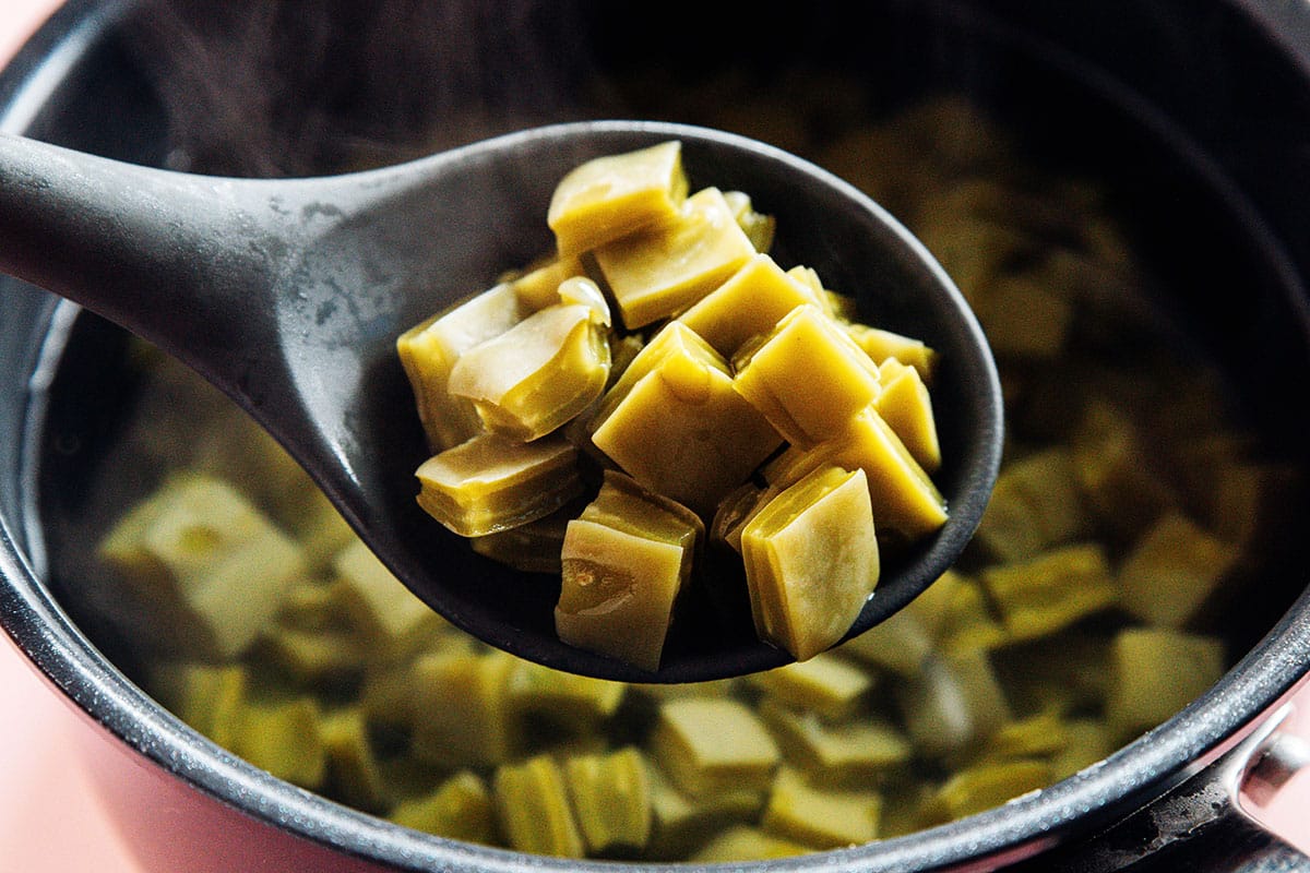 Sliced nopales simmering in a medium pot of water on a home stove with gentle bubbles and steam rising