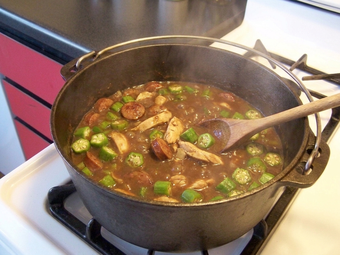 Sliced okra simmering in a pot of chicken and sausage gumbo, with small bubbles breaking the surface