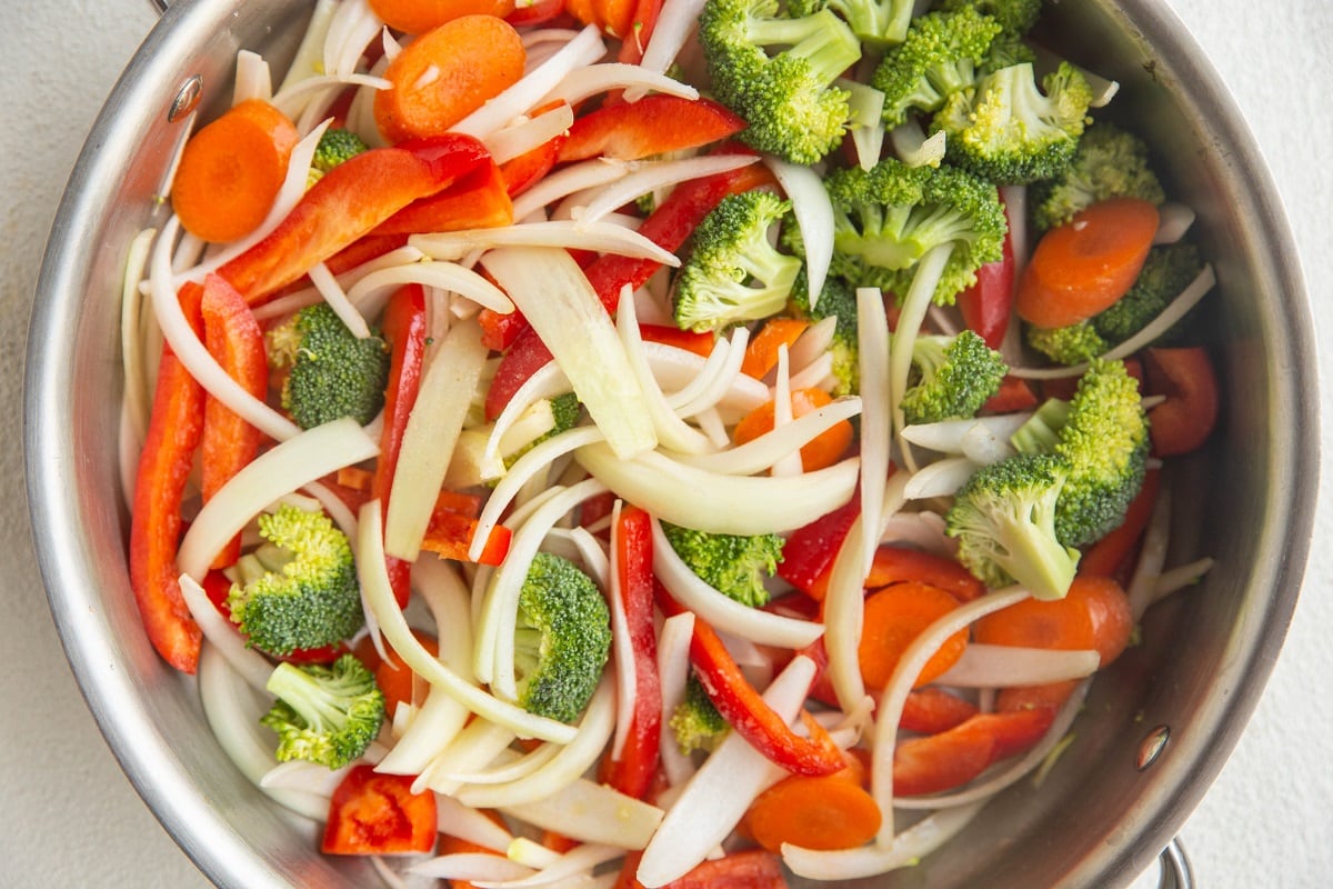 Sliced onion and red bell pepper with chopped garlic and grated ginger prepped in small bowls on a kitchen counter