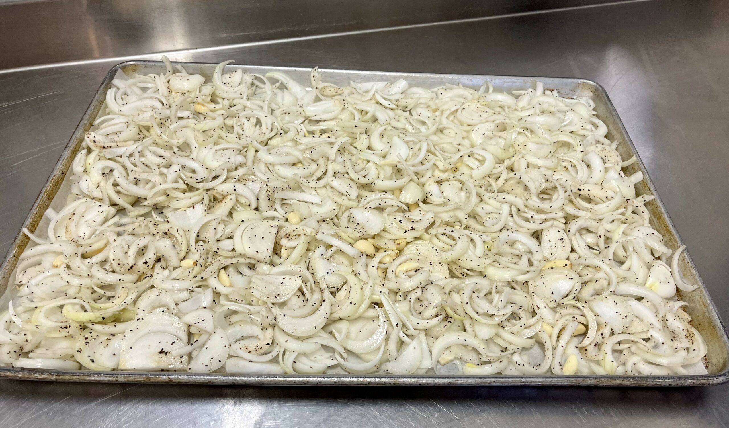 Sliced onions and minced garlic spread across the bottom of a slow cooker insert on a clean home-kitchen counter