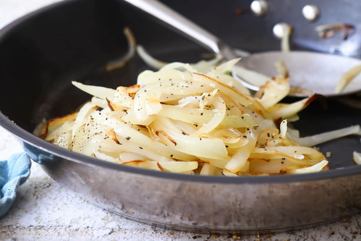 Sliced onions sautéing in olive oil in a large skillet on a home stove, just beginning to turn translucent