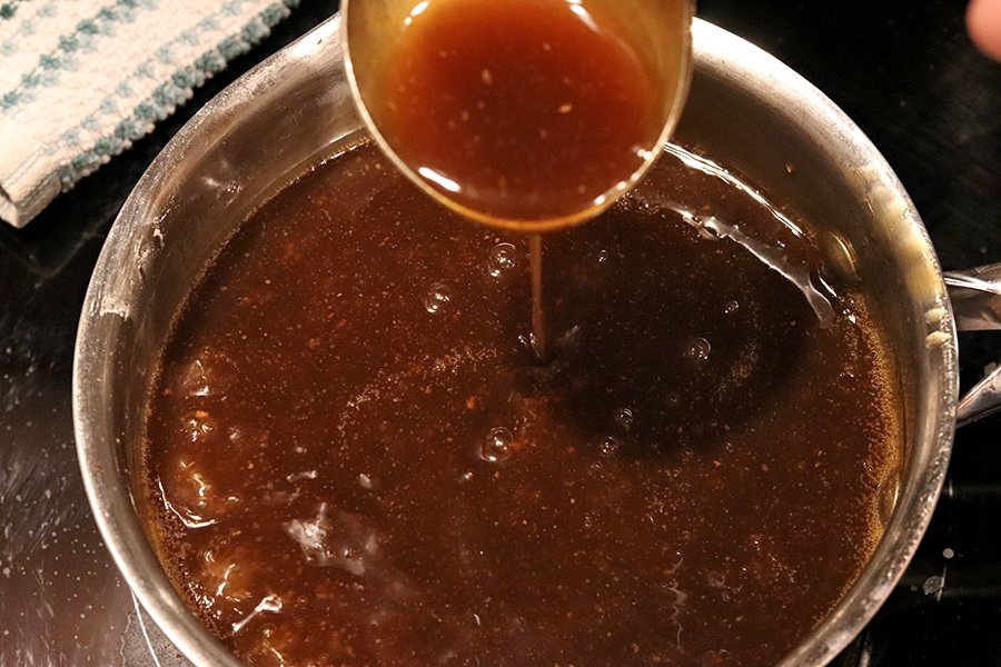Sliced roast beef stored in a glass meal prep container with brown gravy, sitting on a kitchen counter with a lid nearby