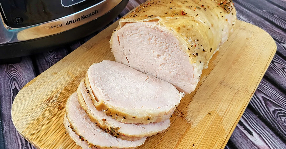 Sliced slow cooker turkey breast fanned on a white platter with herb-flecked gravy in a small pitcher, warm kitchen lighting