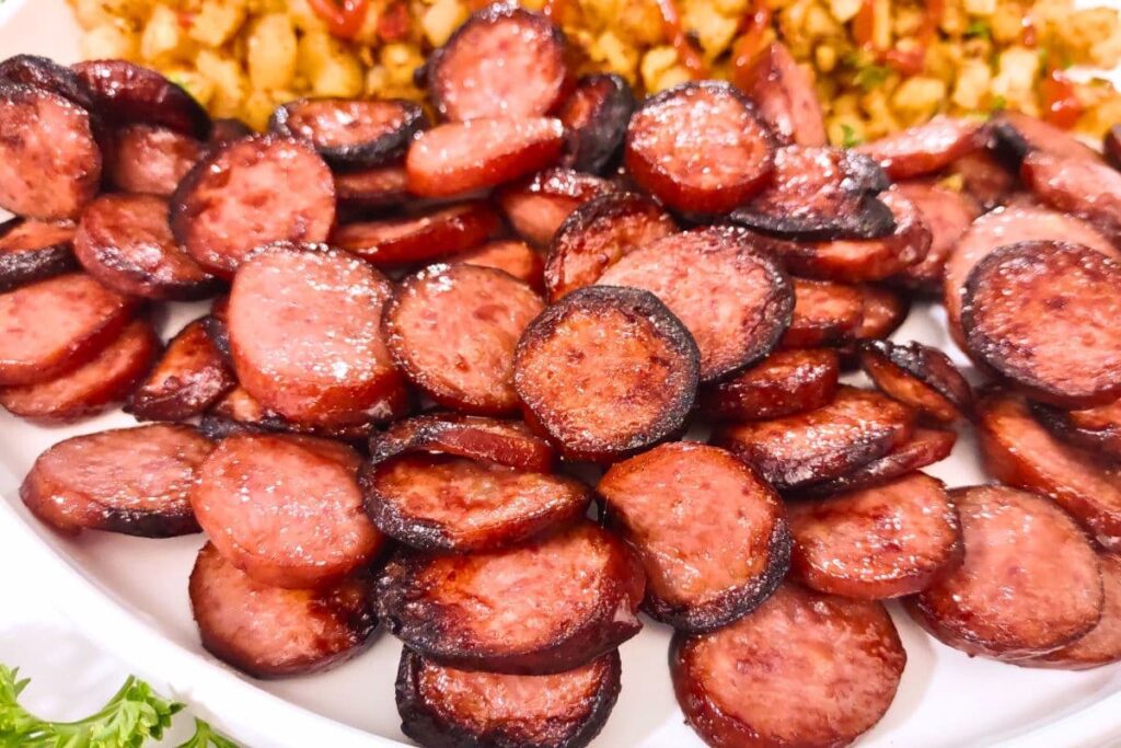 Sliced smoked sausage browning in a cast-iron skillet with caramelized edges forming on the surface