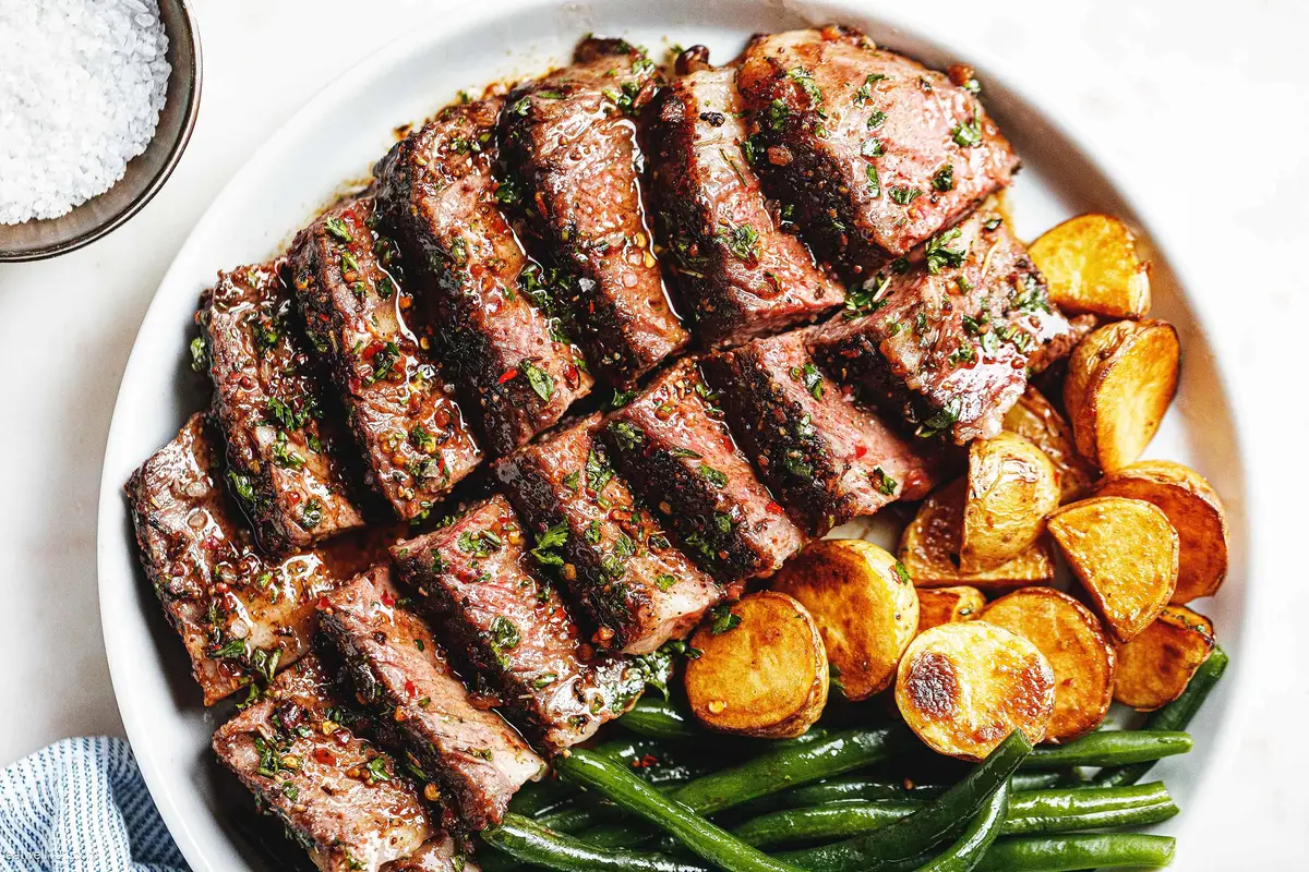 Sliced top round steak fanned on a plate with a glossy garlic butter pan sauce and parsley sprinkled on top, with a fork beside it on a warm kitchen table