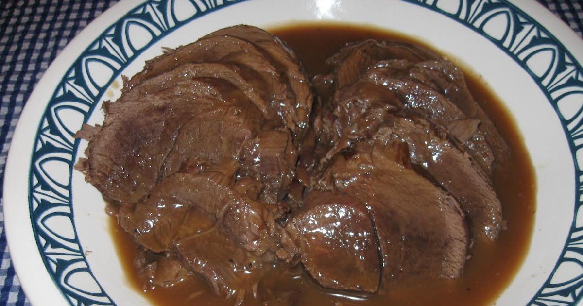 Sliced venison in a glass meal prep container with a ladle of gravy over the top, sitting on a kitchen counter next to a lid