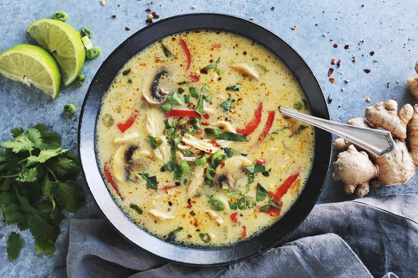 Sliced yellow onion, a spoonful of massaman curry paste, and an open can of coconut milk arranged near a cutting board on a home kitchen counter