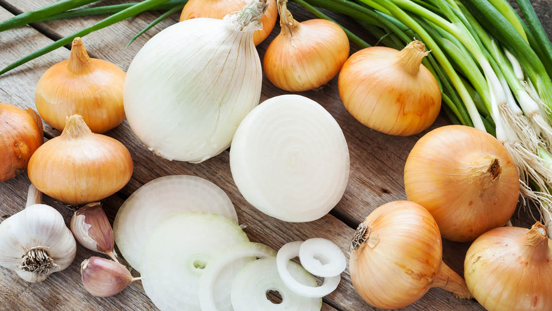 Sliced yellow onion and smashed garlic cloves on a cutting board