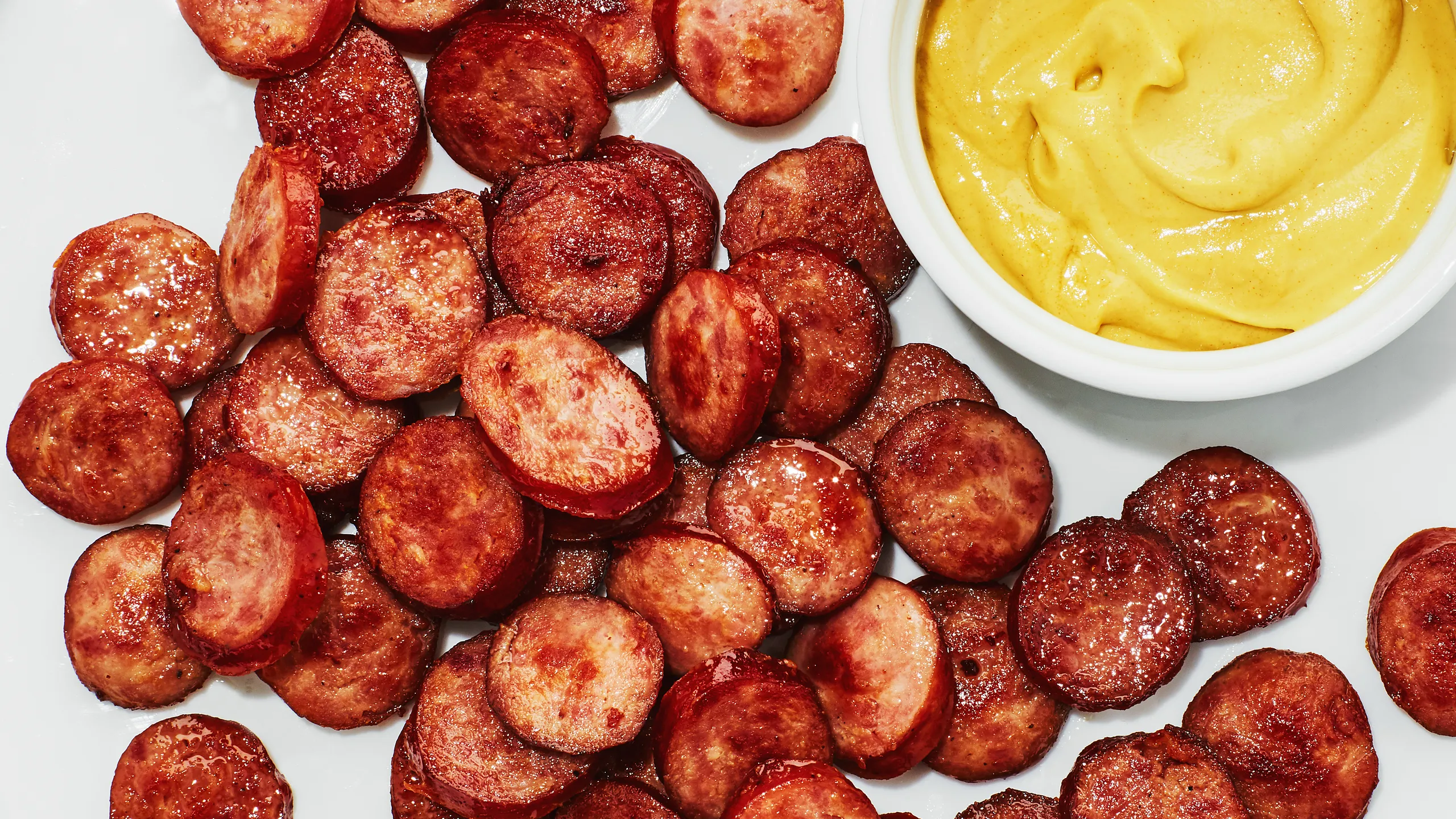 Slices of Polska sausage browning in a hot cast iron skillet with crisp golden edges on a home stove