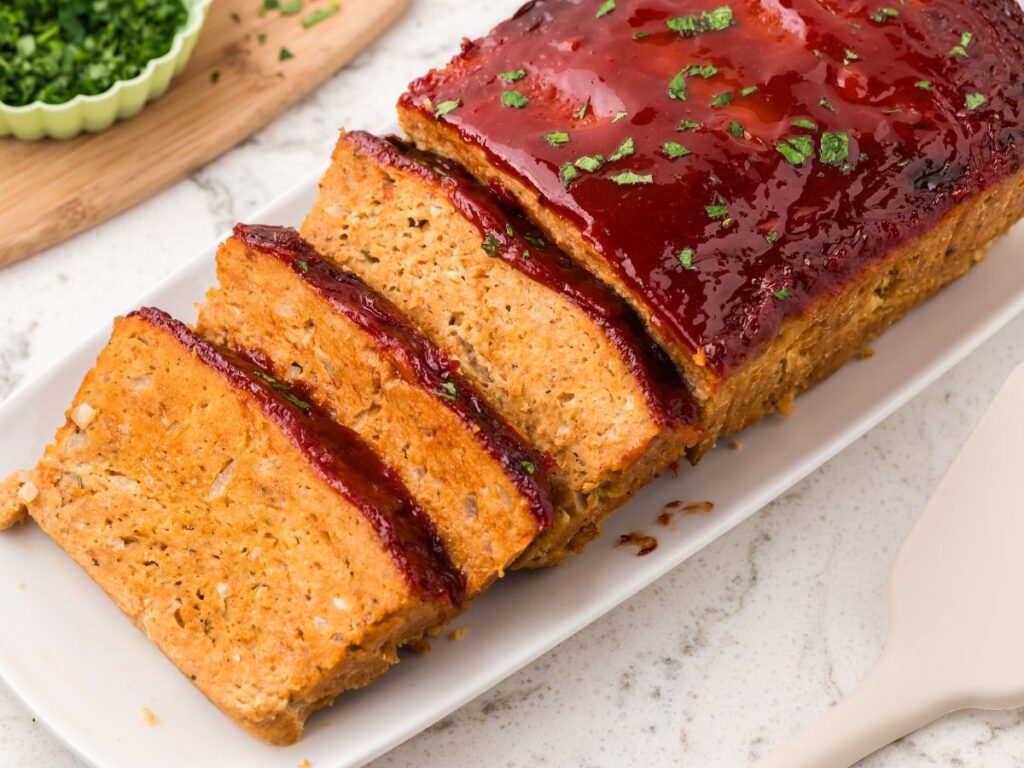 Slices of chicken meatloaf neatly stored in a glass food container with a snap-on lid on a kitchen counter