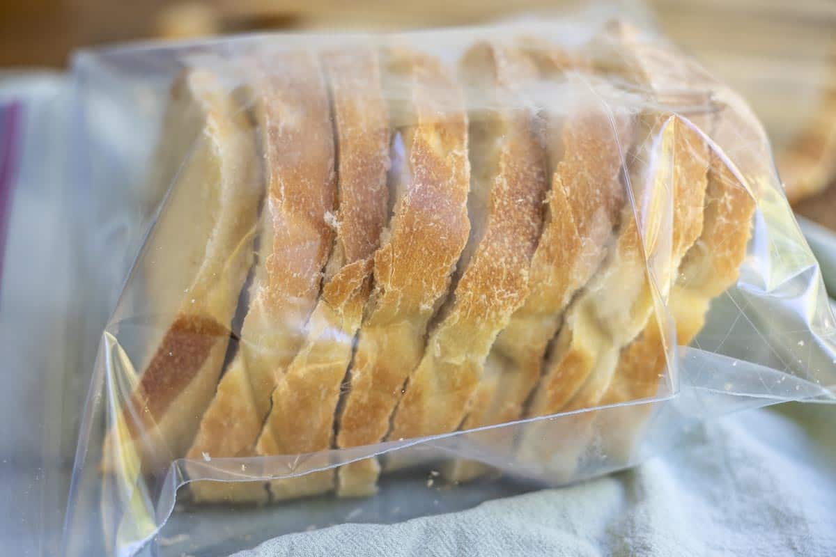 Slices of homemade sandwich bread stacked in a clear freezer bag on a kitchen counter, ready for freezing