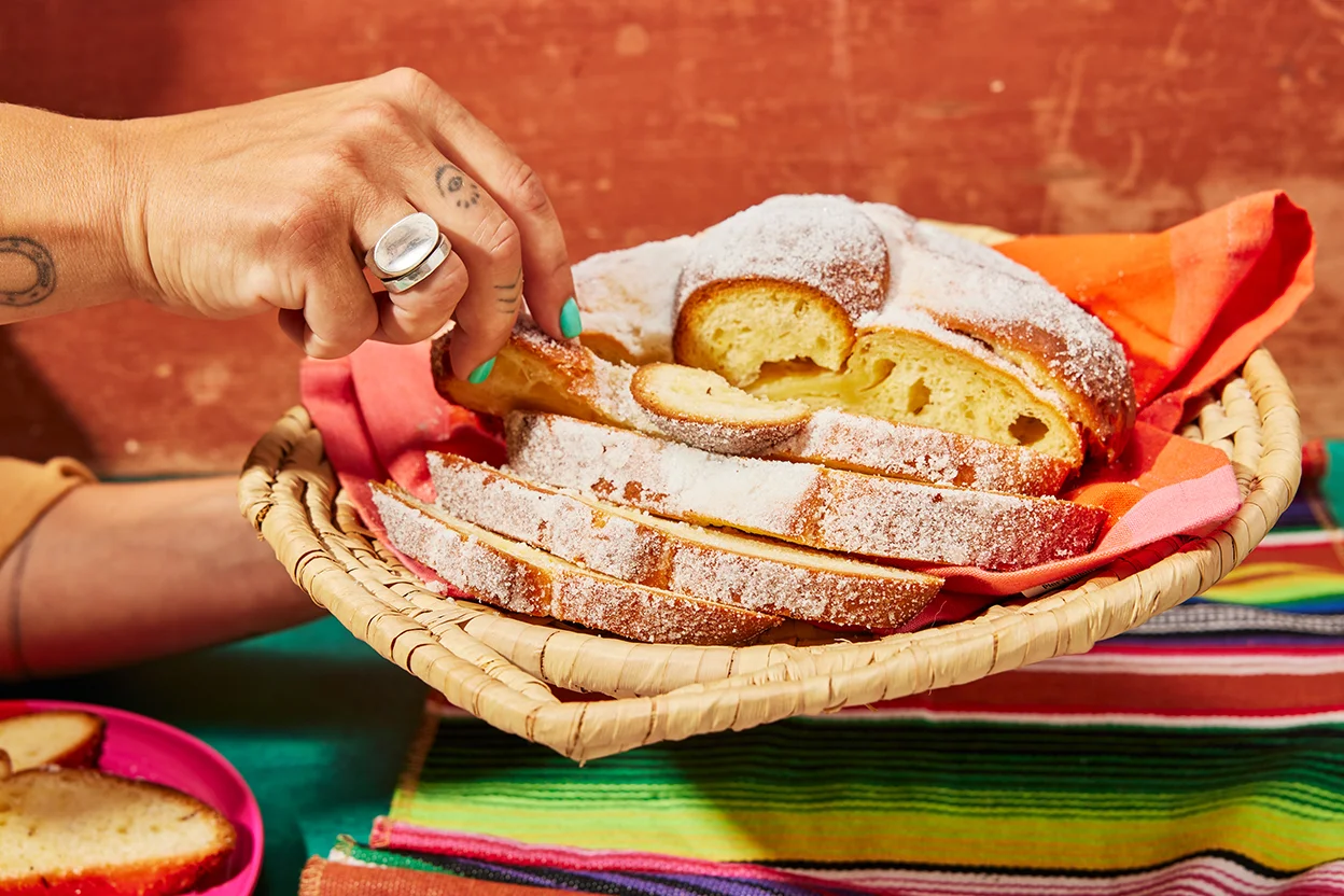 Slices of pan de muerto on a small ceramic plate with a light sugar dusting, next to a mug on a wooden table
