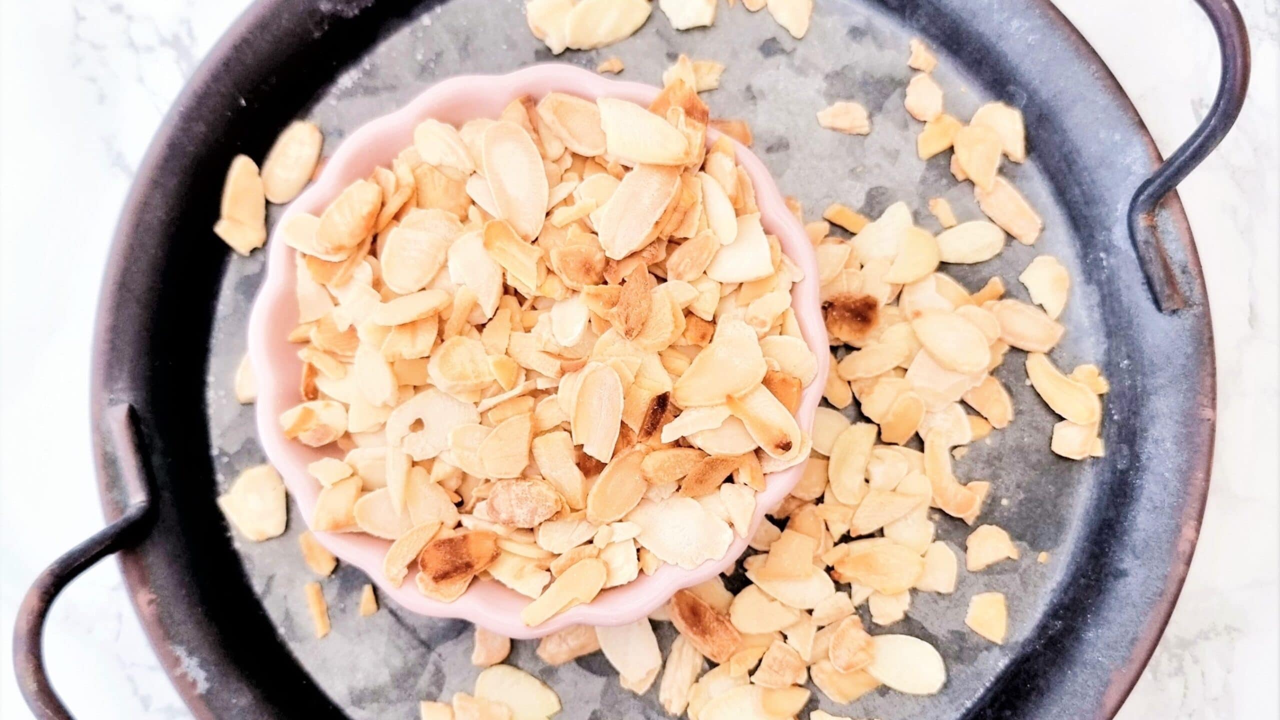 Slivered almonds toasting in a small skillet on a stovetop until lightly golden