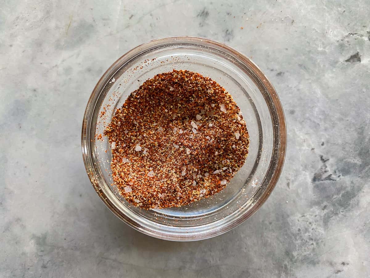 Small bowl of mixed dried herbs, salt, pepper, and paprika beside turkey tenderloins ready to be seasoned on a kitchen counter