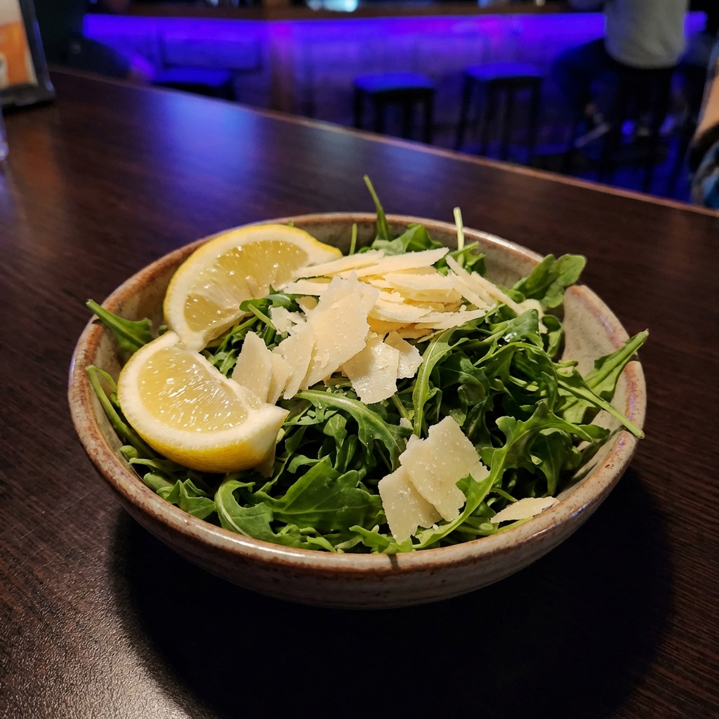 Small bowl of simple arugula salad with lemon wedges and shaved Parmesan