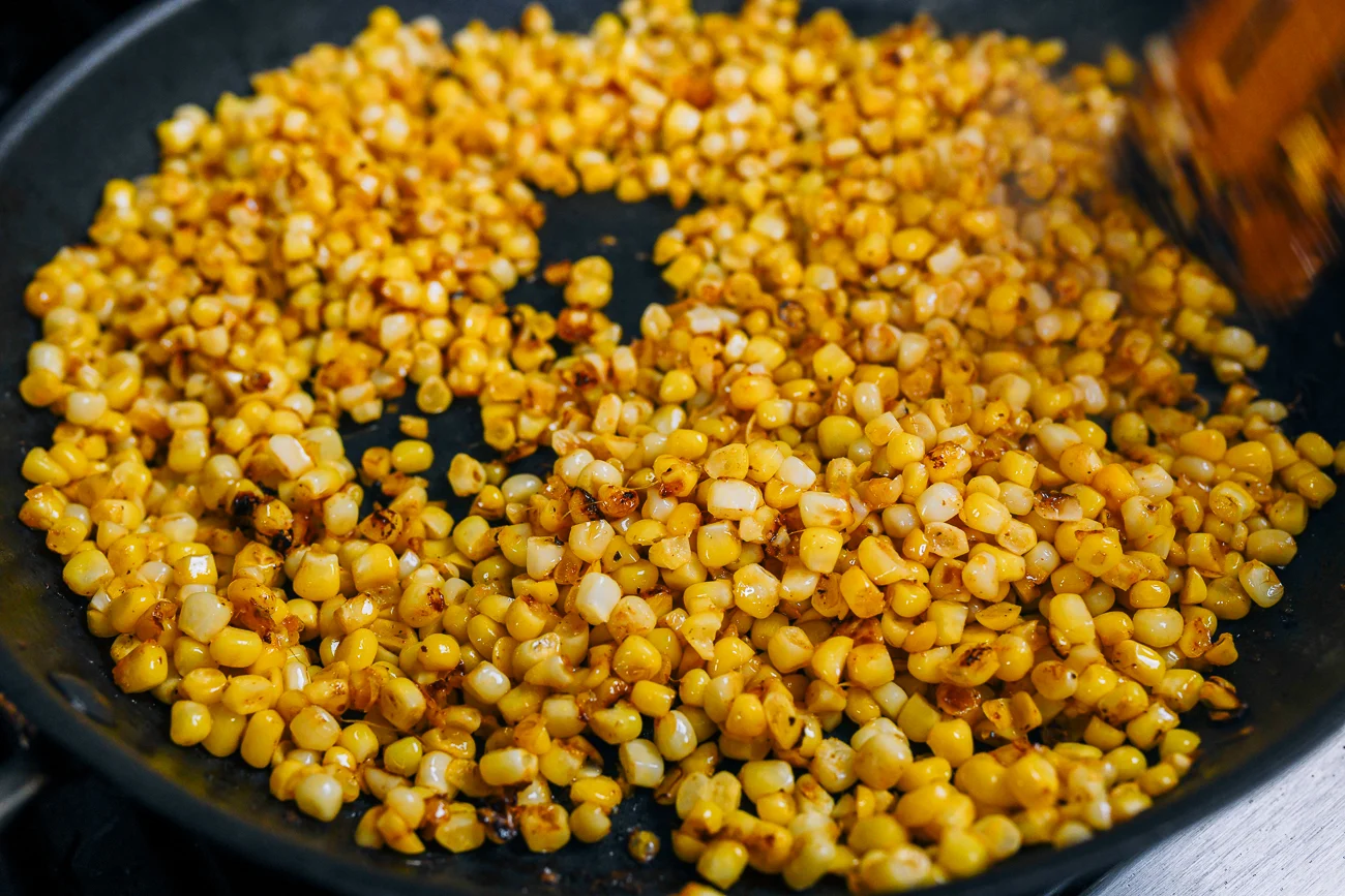 Small bowls of corn kernels, butter, diced onion, garlic, paprika, salt, black pepper, and a halved lime arranged on a clean kitchen counter