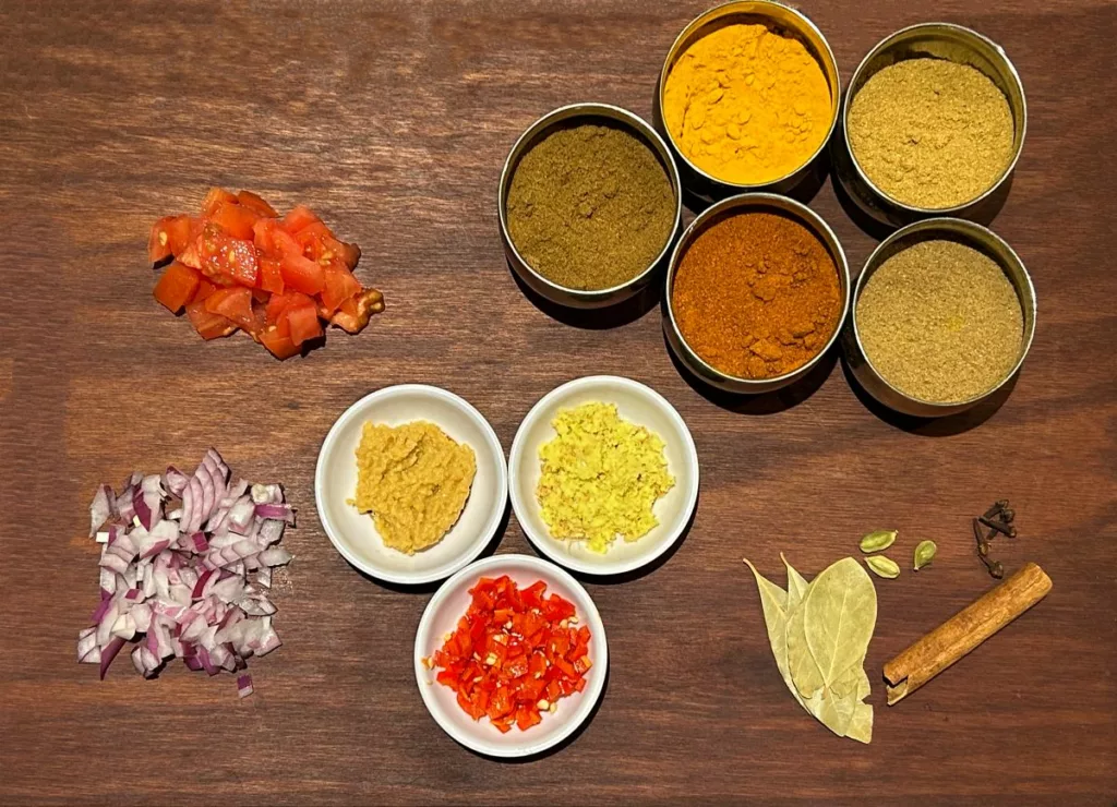 Small bowls of garam masala, cumin, paprika, and turmeric measured out on a kitchen counter beside a spoon