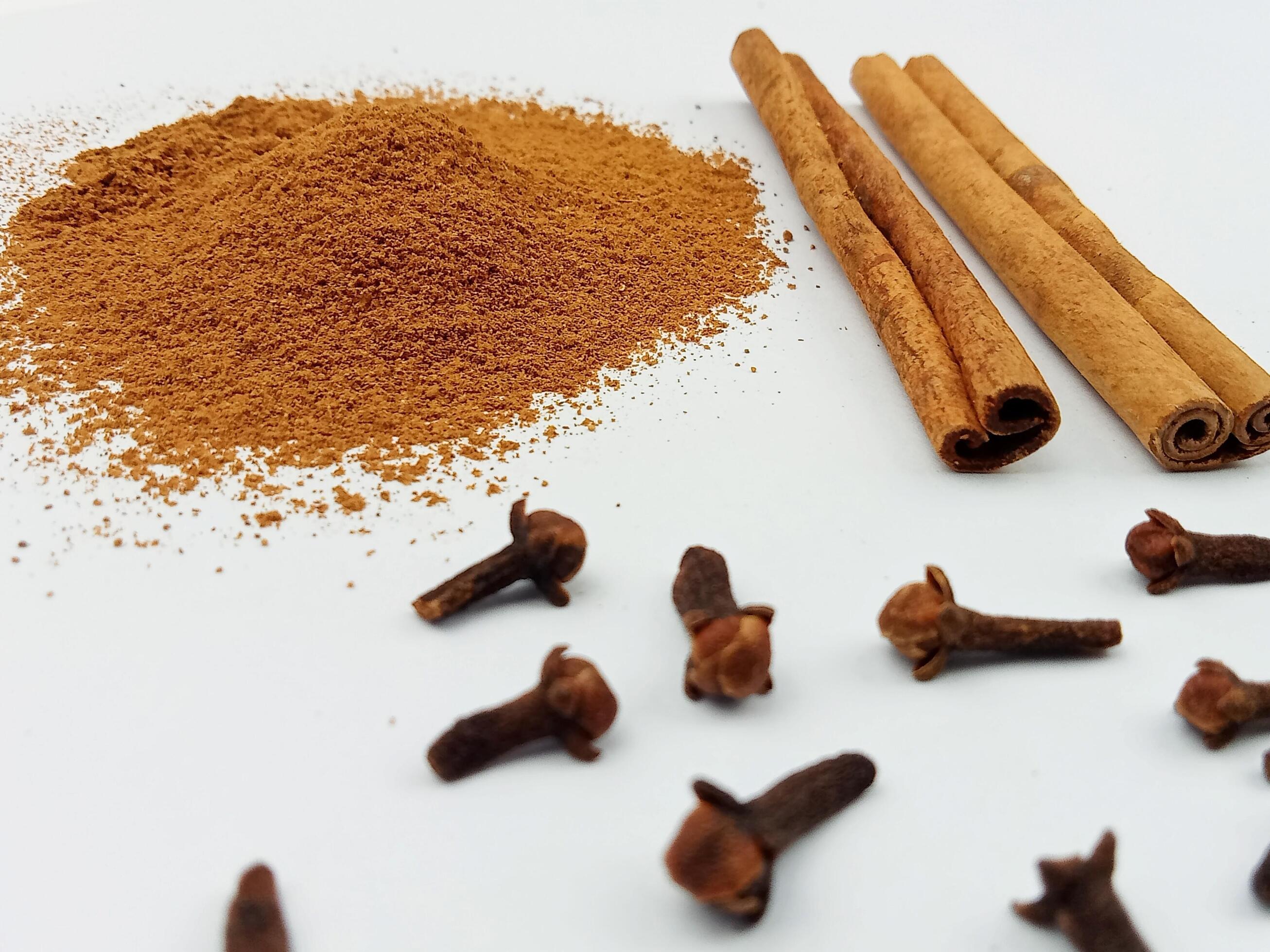 Small bowls of ground cinnamon and ground cloves on a kitchen counter with measuring spoons nearby