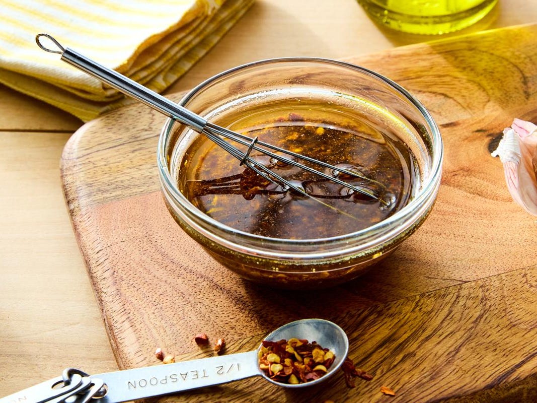 Small bowls of lime juice, orange juice, oil, minced garlic, cumin, chili powder, paprika, oregano, salt, and pepper arranged on a kitchen counter
