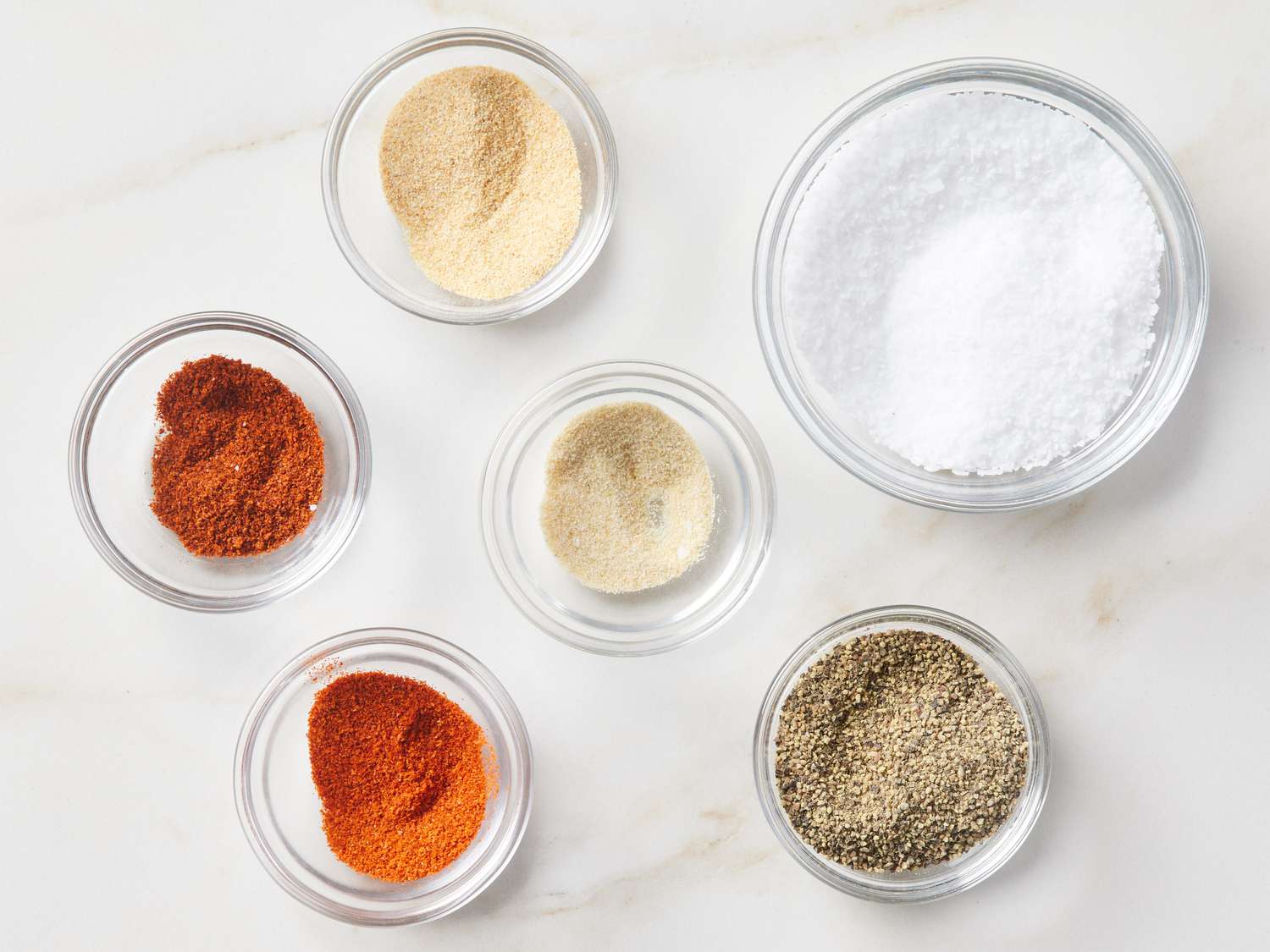 Small bowls of seasonings like garlic powder, paprika, and black pepper next to a container of cottage cheese on a clean kitchen counter