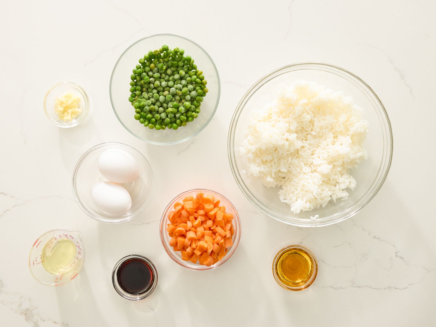 Small bowls of soy sauce, minced ginger, garlic, frozen peas and carrots, cooked rice, and sliced pork tenderloin arranged on a kitchen counter