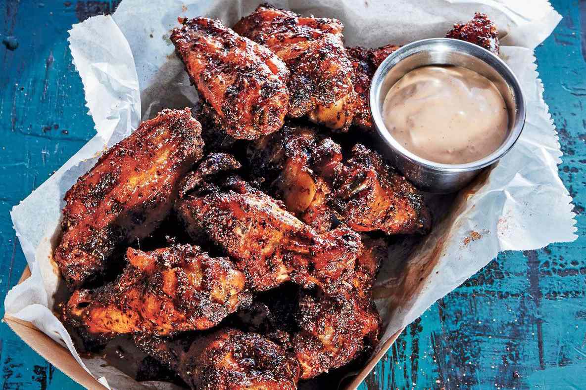 Small bowls of spices including smoked paprika, garlic powder, brown sugar, black pepper, and baking powder arranged on a kitchen counter next to a bowl of raw chicken wings