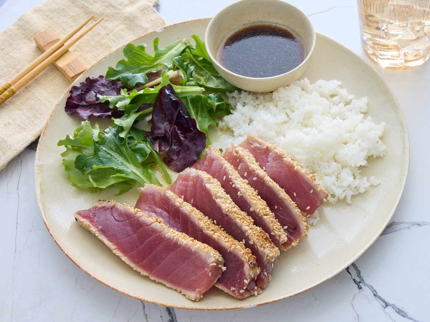 Small bowls of white and black sesame seeds with soy sauce and lime beside raw ahi tuna steaks on a cutting board