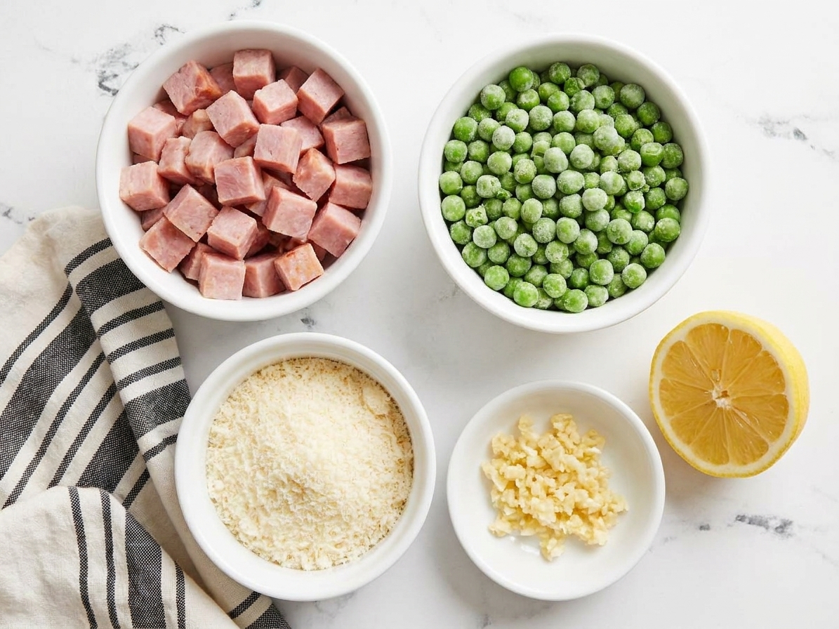 Small bowls on a kitchen counter holding diced cooked ham, frozen peas, grated Parmesan, minced garlic, and a halved lemon ready for cooking