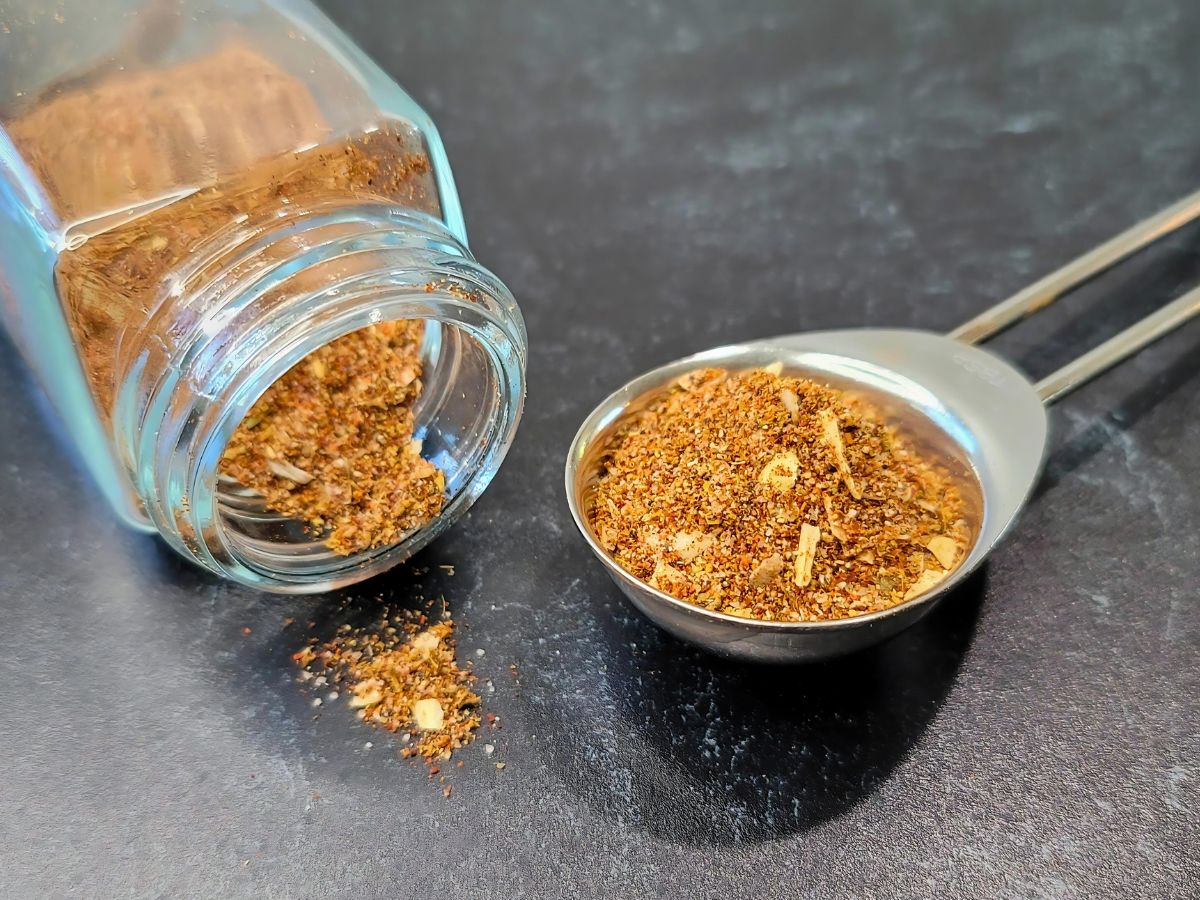 Small ceramic bowls of chili powder, cumin, smoked paprika, garlic powder, and oregano arranged on a kitchen counter before mixing