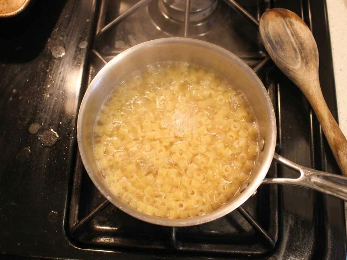 Small pasta boiling in a small pot of water on the stove with light steam rising