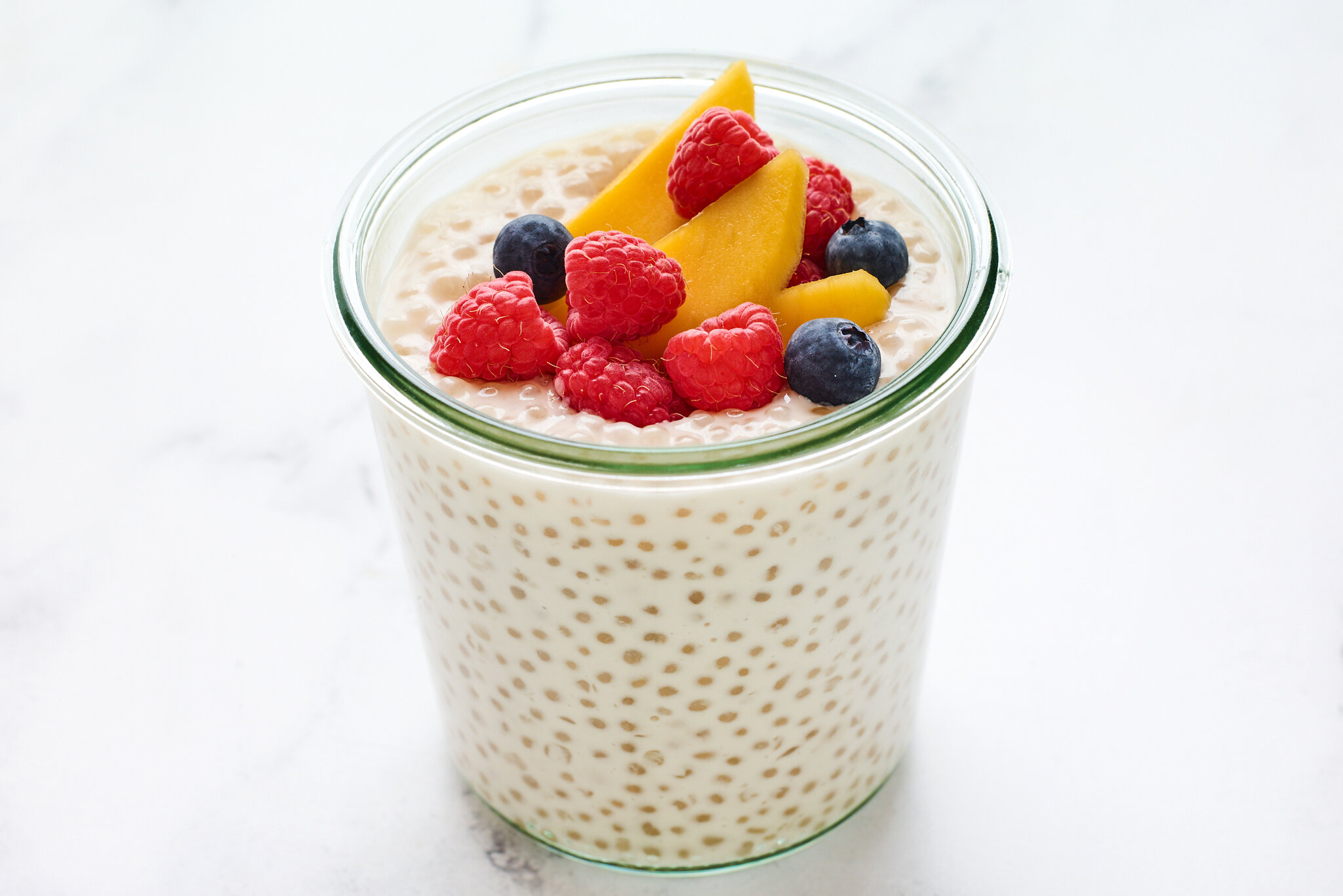 Small sago pearls simmering in a medium saucepan on a stovetop with a spoon stirring to prevent sticking