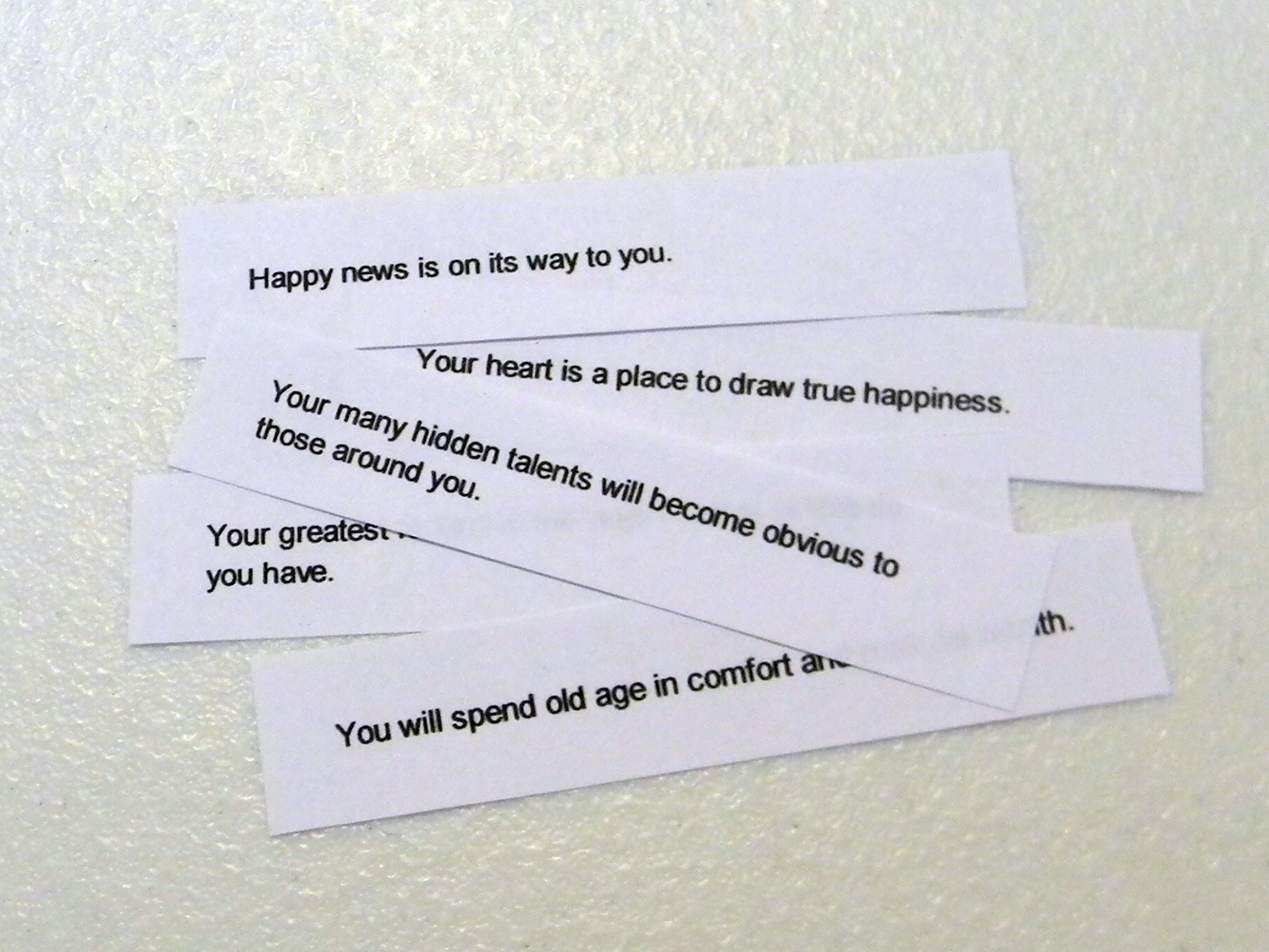 Small strips of clean, plain paper fortunes laid out in a neat row on a wooden cutting board