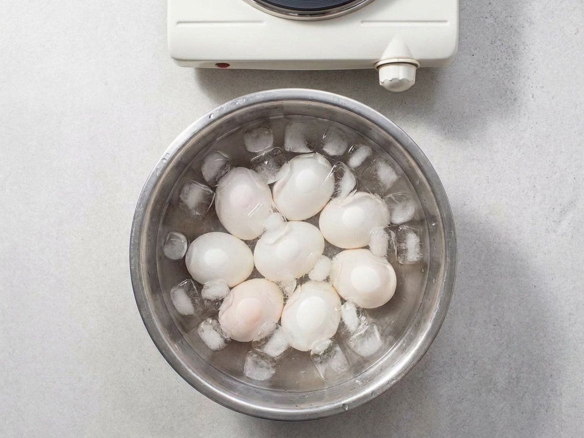 Soft-boiled eggs cooling in an ice bath in a metal mixing bowl on a kitchen counter
